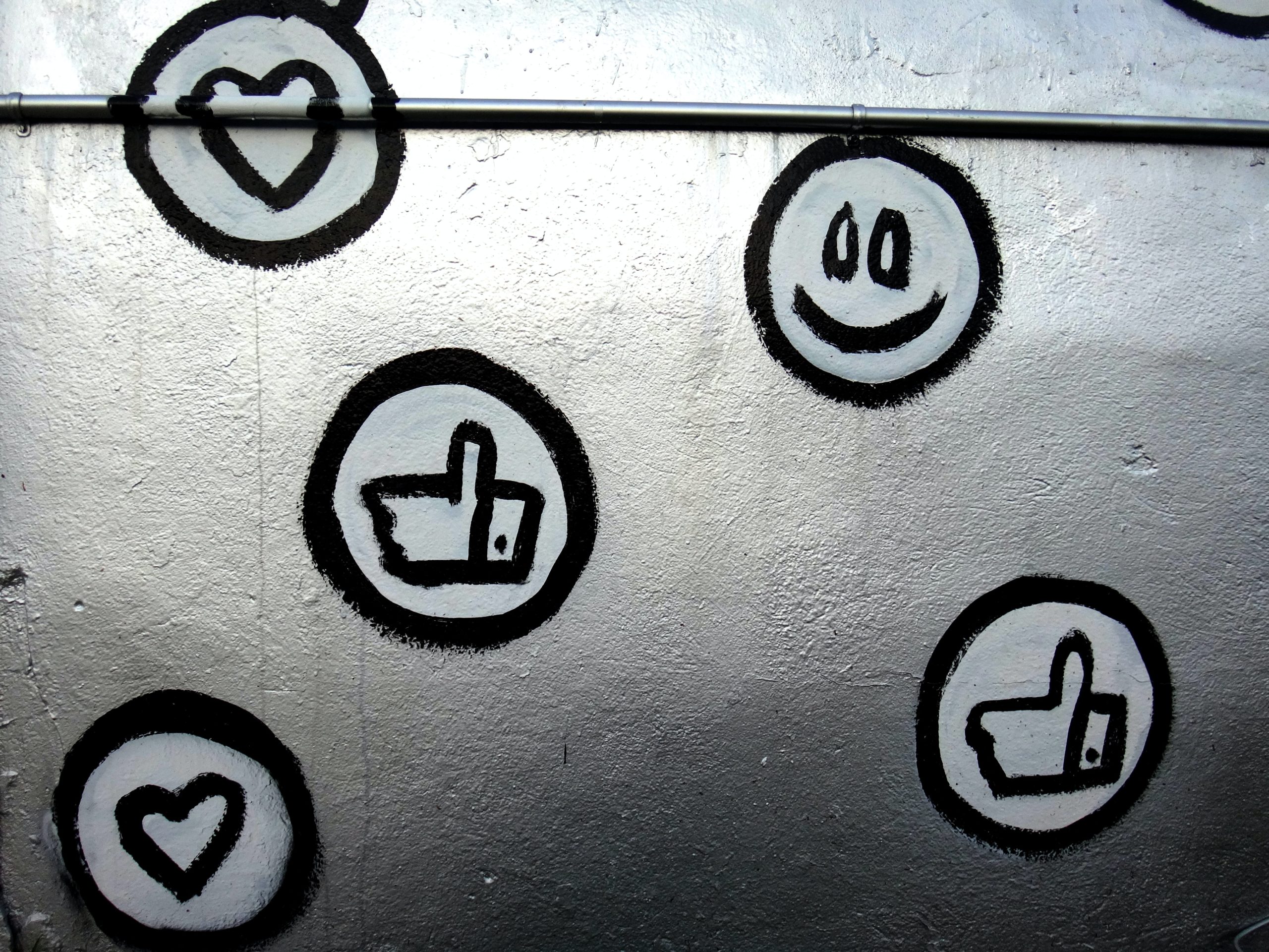 A decorative image of a smiley face and social media reaction buttons, such as a like and heart, spray painted onto a wall.